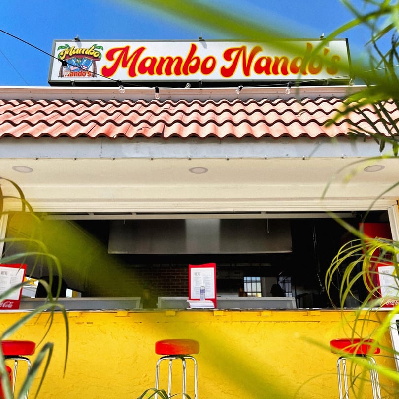 Mambo Nando's restaurant exterior with a yellow counter, red stools, and a tiled roof.
