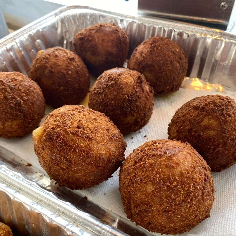 Eight golden-brown, breaded alcapurrias, a Puerto Rican fritter, resting in a foil pan.