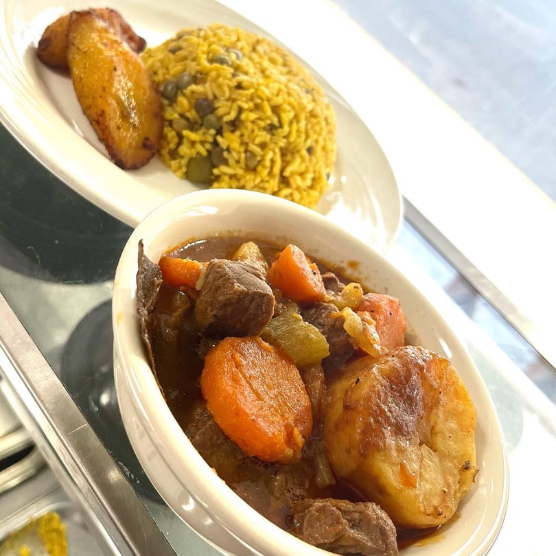Mambo Nando's Puerto Rican beef stew with carrots and potatoes, alongside yellow rice and plantains.