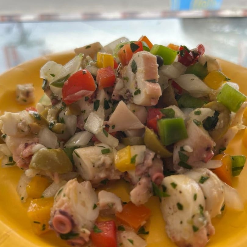 Mambo Nando's octopus salad with colorful peppers, onions, and olives on a yellow plate.