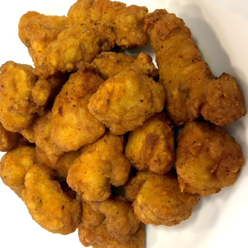 Close-up of a pile of golden-brown, crispy fried chicken pieces on a white plate.